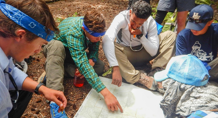 a group of people examine a map that is spread out on the ground